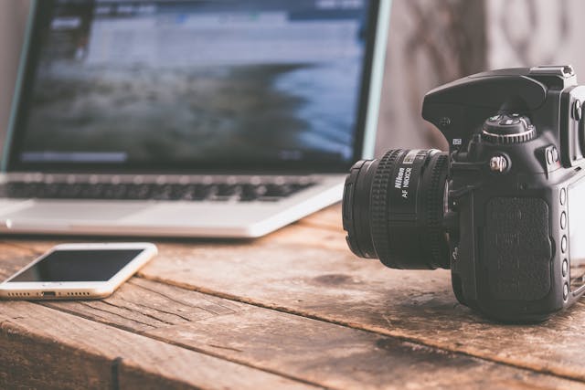 a camera, cellphone and a compter on a wooden table