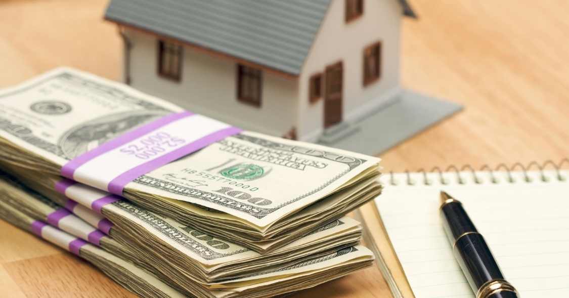 a stack of cash next to a home figurine